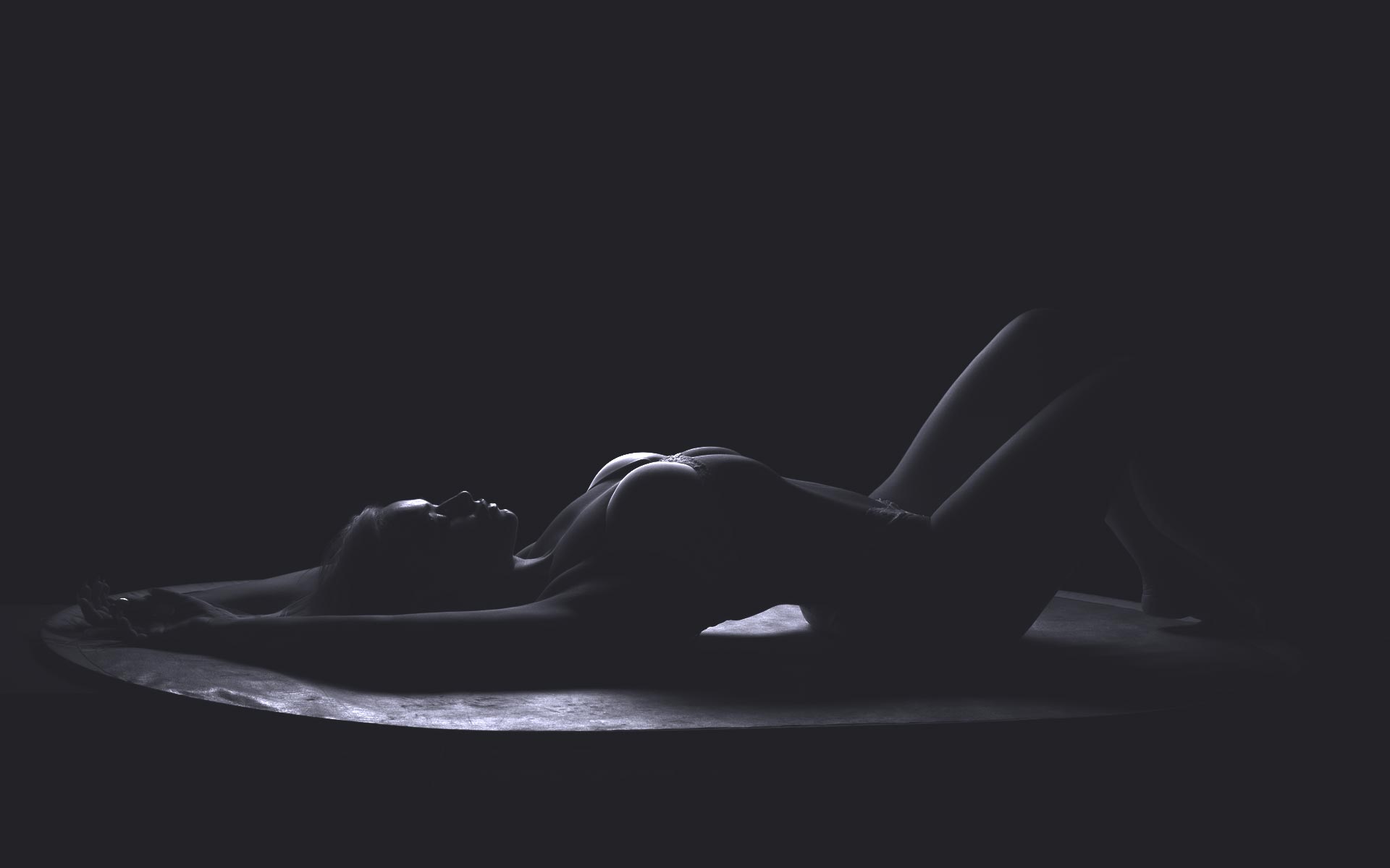 A silhouette of a woman lying on her back in a dimly lit setting, with subtle highlights contouring her figure as she begins to awaken.